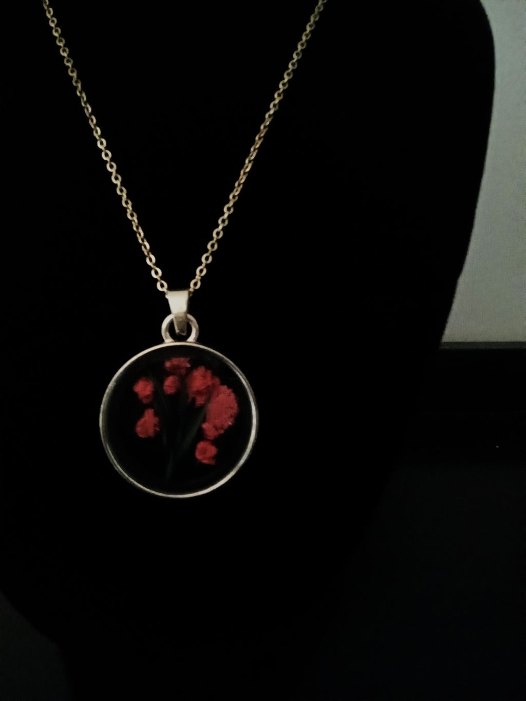 A gold-toned chain necklace with a round pendant featuring fuchsia flowers.