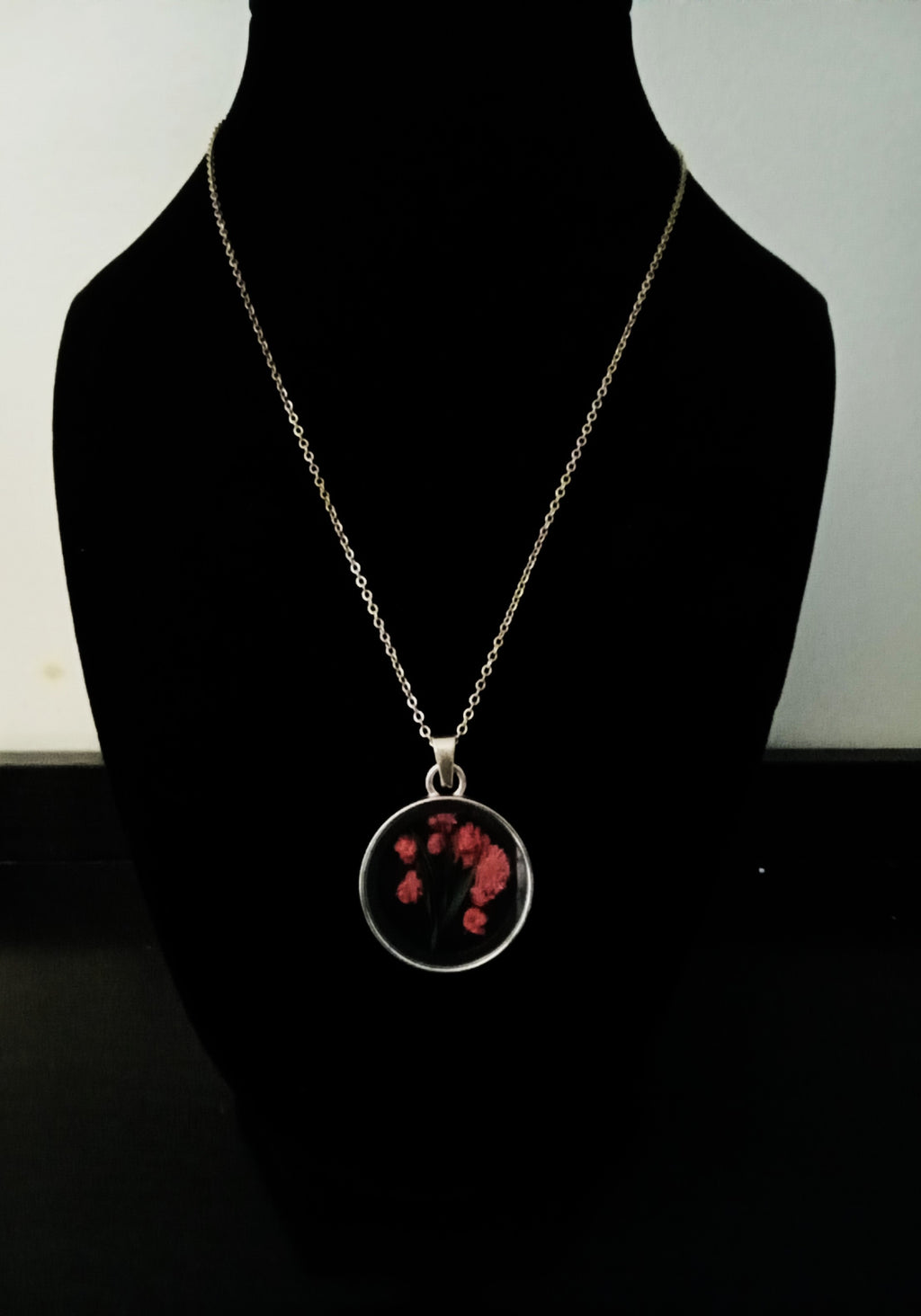 A gold chain necklace with a round pendant featuring fuchsia flowers.
