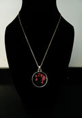 A gold chain necklace with a round pendant featuring fuchsia flowers.