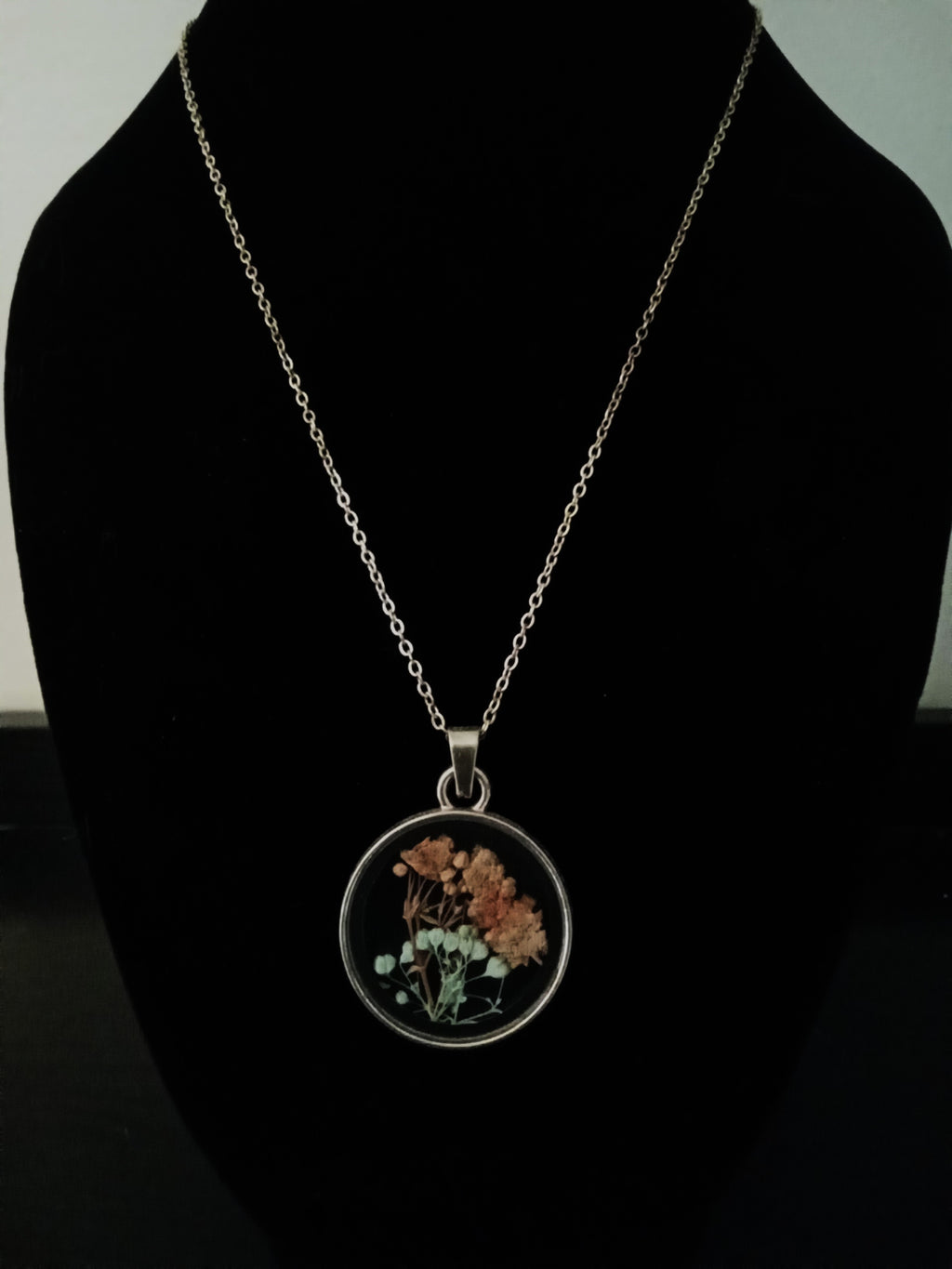 A gold chain necklace with a round pendant displaying dried orange flowers and green leaves.