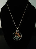 A gold chain necklace with a round pendant displaying dried orange flowers and green leaves.