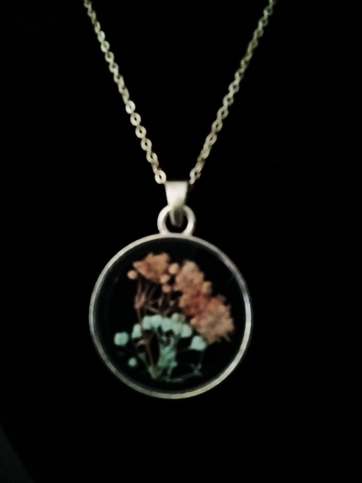A gold chain necklace with a round pendant featuring dried flowers.