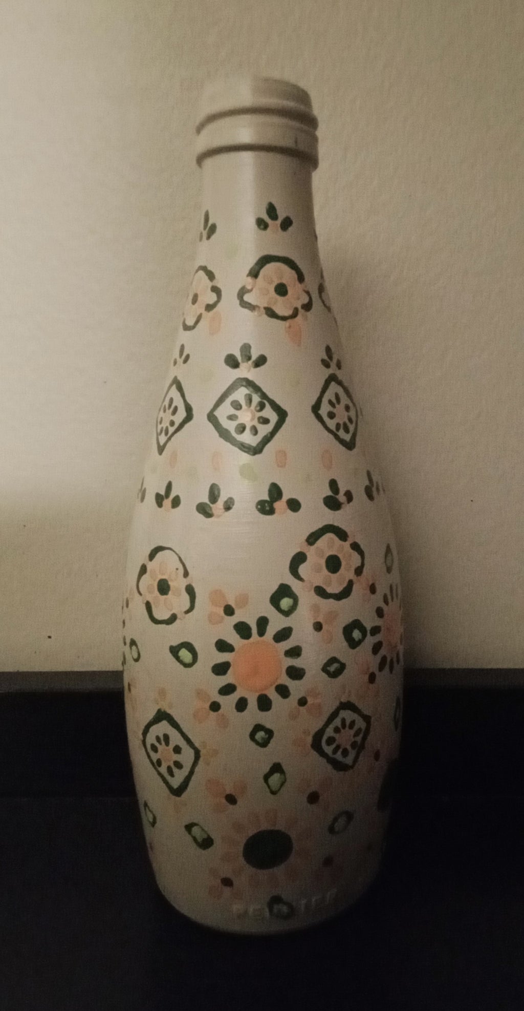 A white glass bottle with a hand-painted folk-art pattern in green and orange.