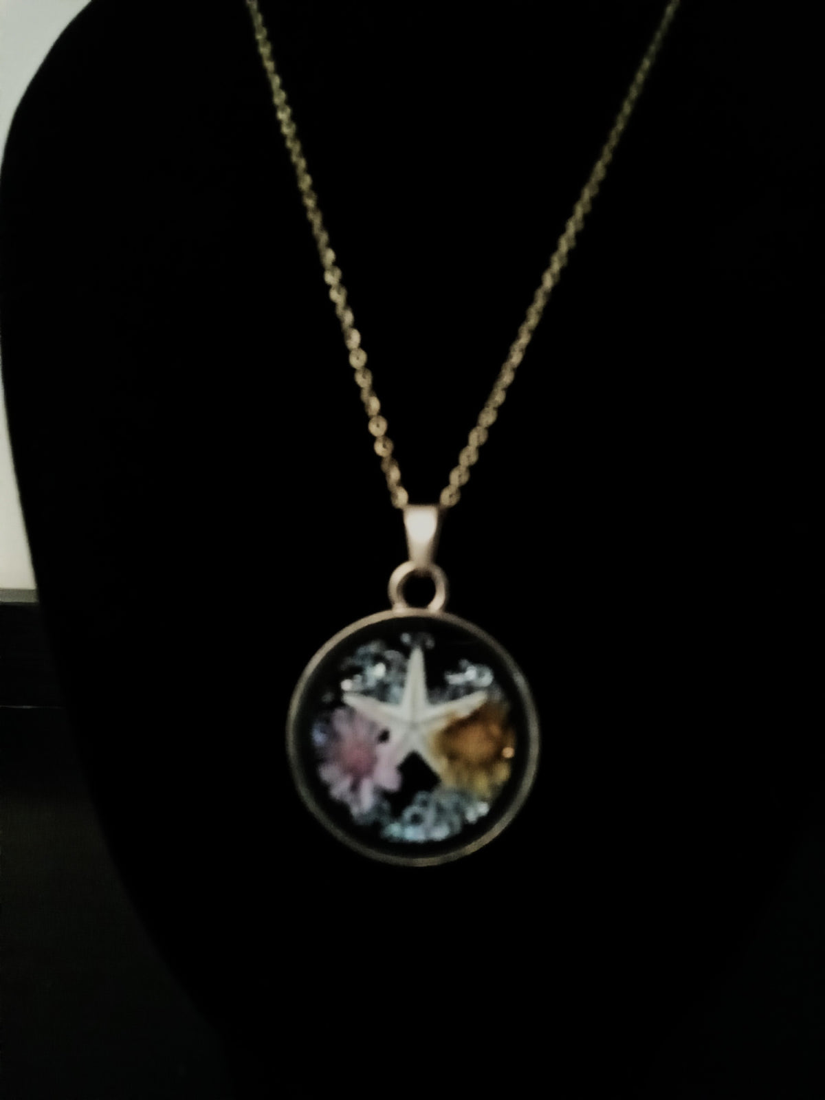 A round pendant necklace featuring a gold-toned starfish design over a multicolored background with pink, blue, and yellow details.