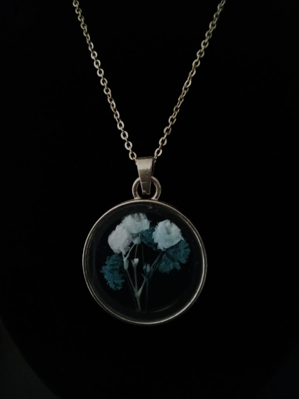 A gold chain necklace with a round pendant featuring pressed white flowers.