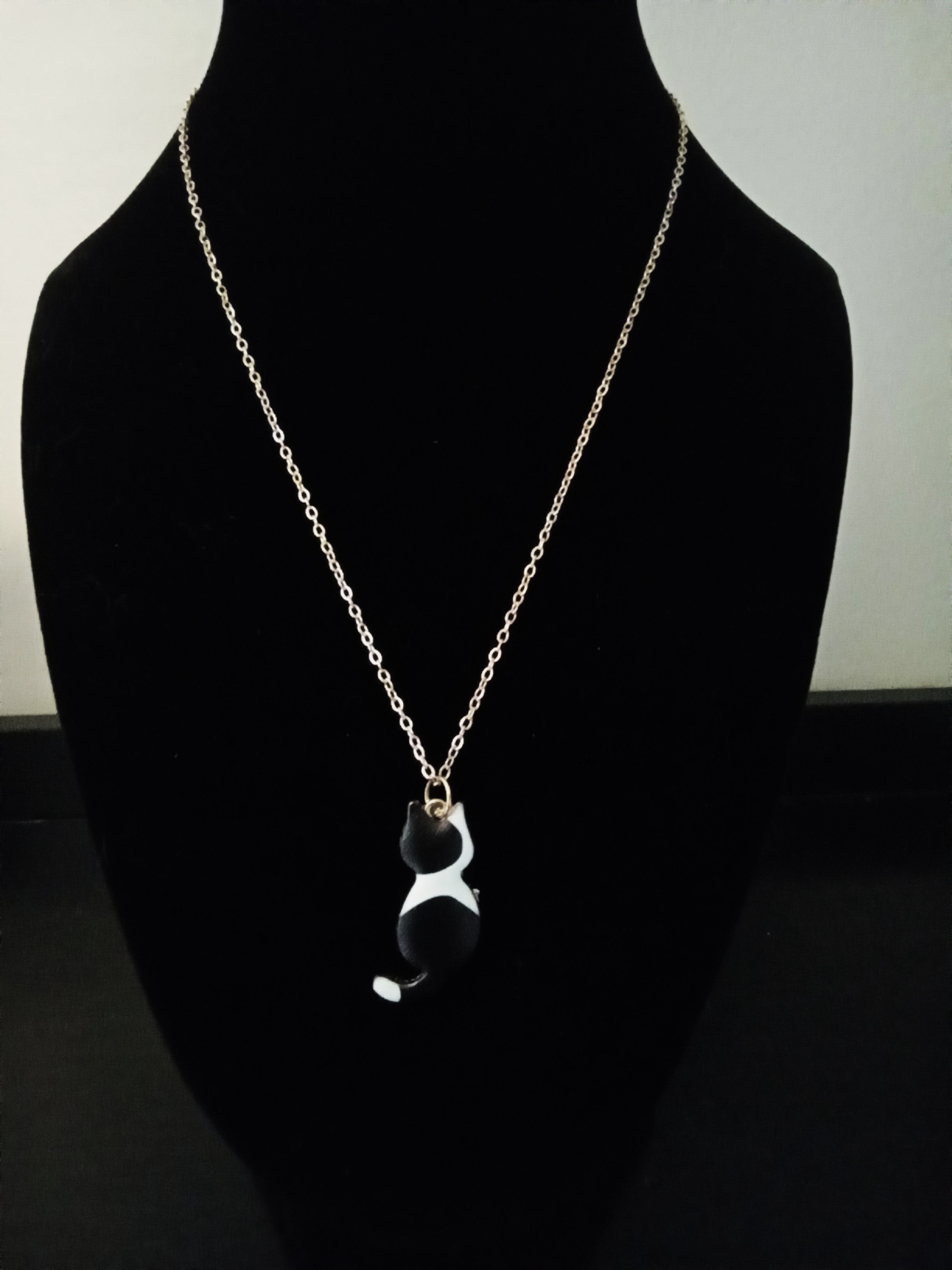 A gold-toned chain necklace with a small black and white cat pendant, displayed on a black velvet mannequin bust.