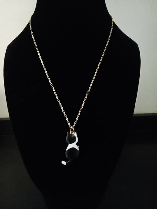 A gold-toned chain necklace with a small black and white cat pendant, displayed on a black velvet mannequin bust.