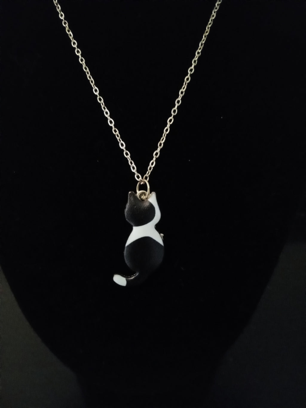 A gold chain necklace featuring a small black and white cat pendant, displayed on a black bust.