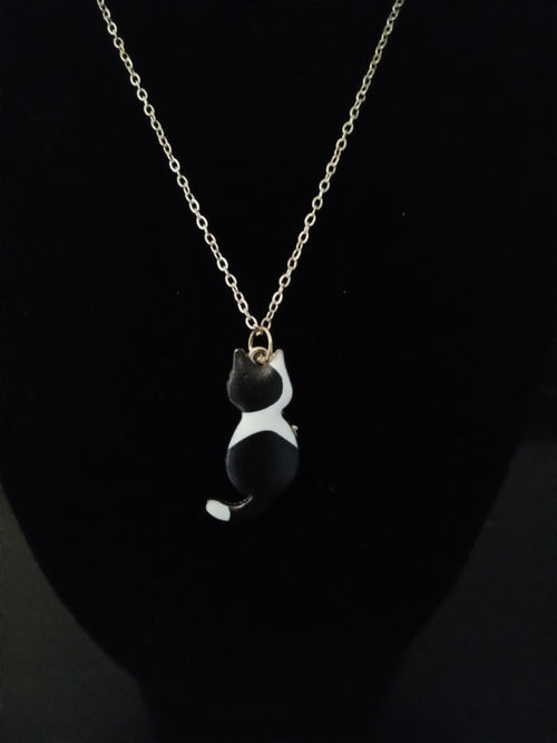A gold chain necklace featuring a small black and white cat pendant, displayed on a black bust.