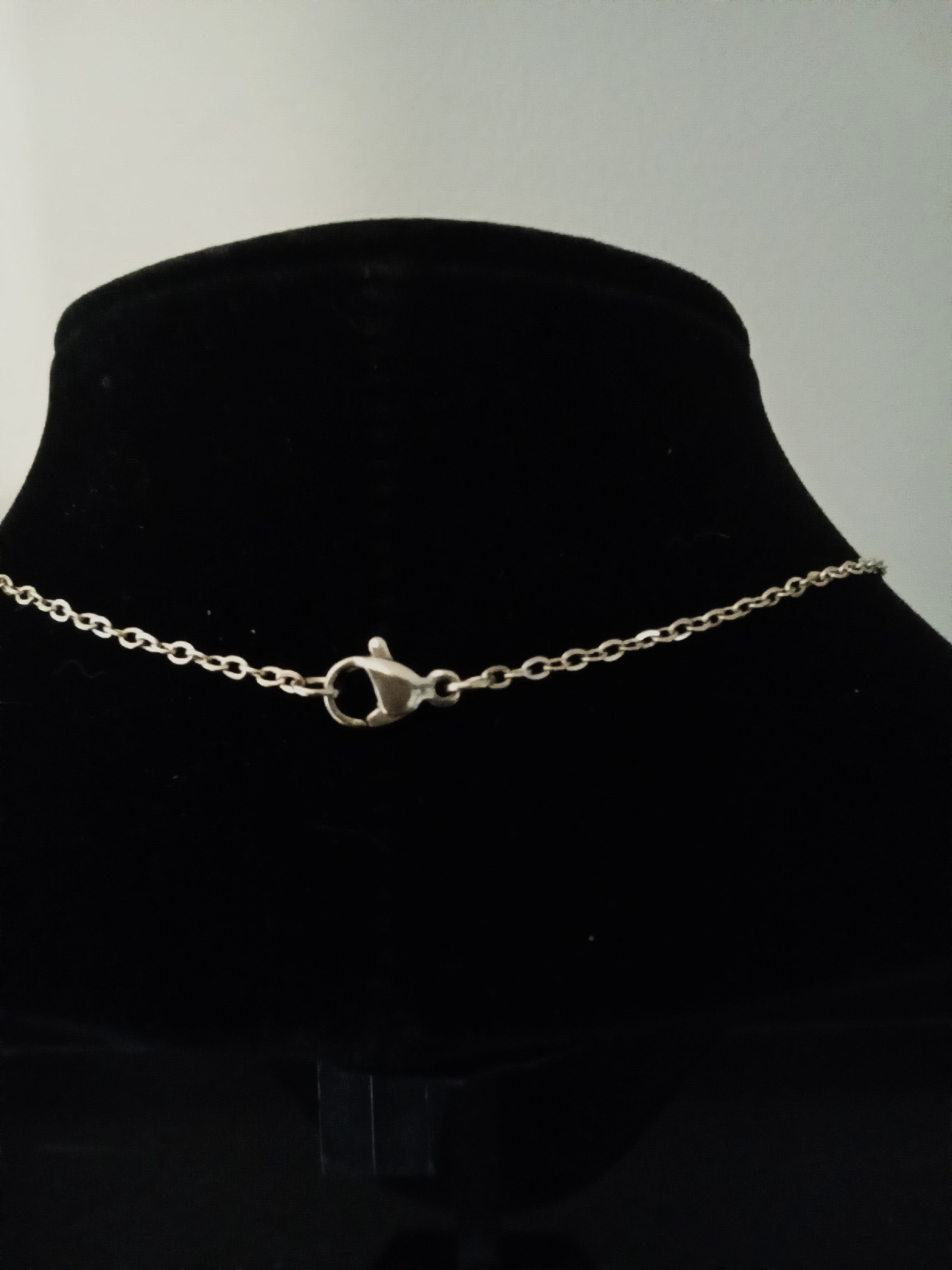 A delicate gold chain necklace with a lobster clasp, displayed on a black velvet jewelry bust.