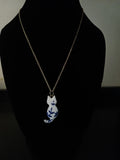 A gold-tone chain necklace with a white cat pendant decorated with blue floral patterns, displayed on a black jewelry bust.