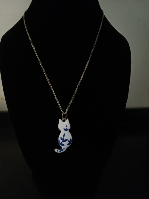 A gold-tone chain necklace with a white cat pendant decorated with blue floral patterns, displayed on a black jewelry bust.