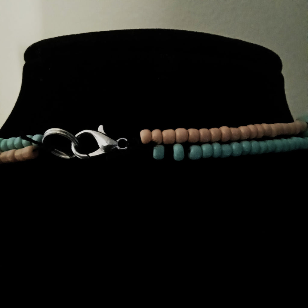 A beaded necklace with turquoise blue and light orange beads, featuring a silver lobster clasp, displayed on a black velvet jewelry bust.
