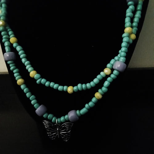 A double-strand beaded necklace displayed on a black jewelry bust. The necklace features turquoise-colored beads, small yellow accent beads, lavender-purple spacer beads, and a silver butterfly pendant at the center.