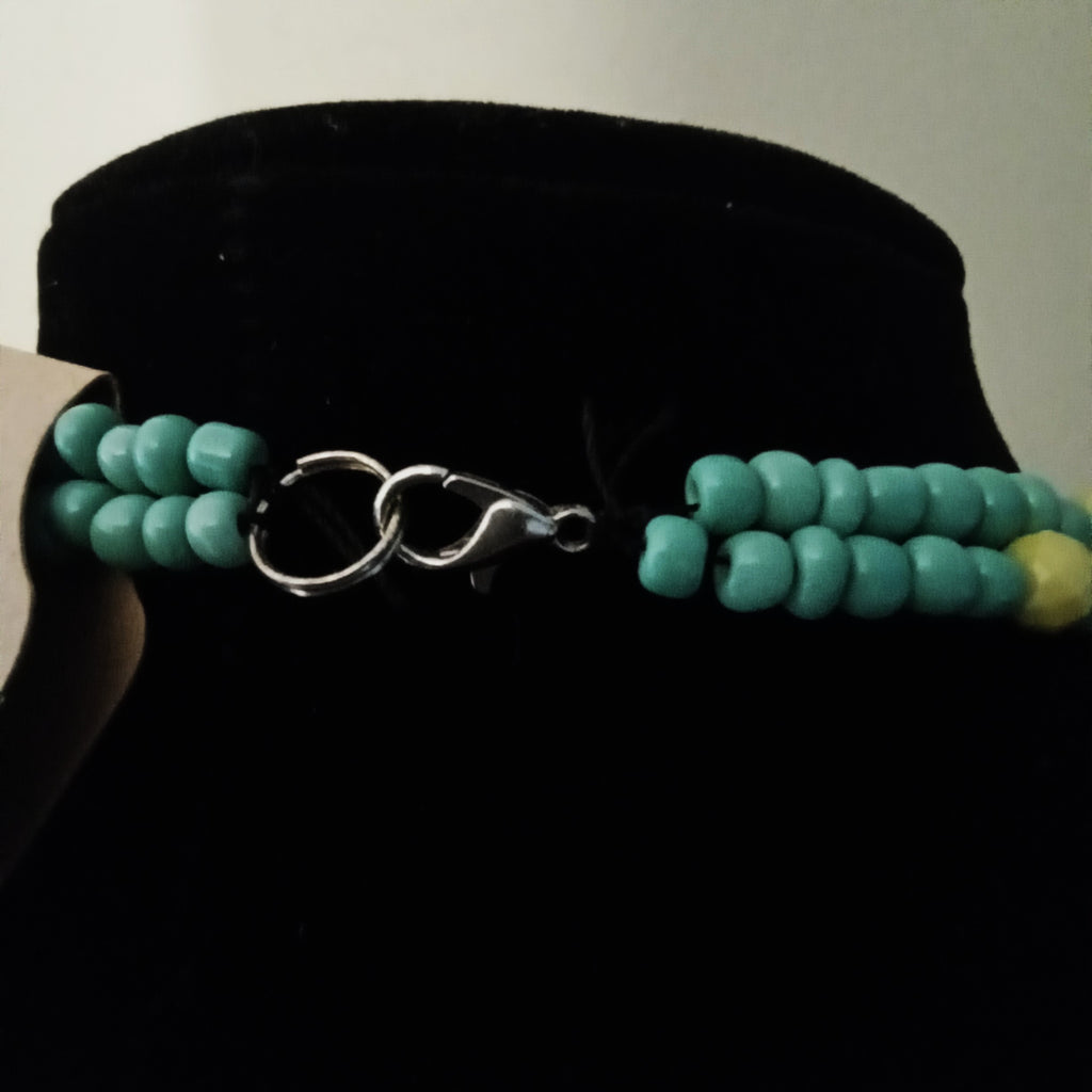 A beaded necklace with turquoise-colored round beads and a silver lobster clasp, displayed on a black velvet jewelry bust.