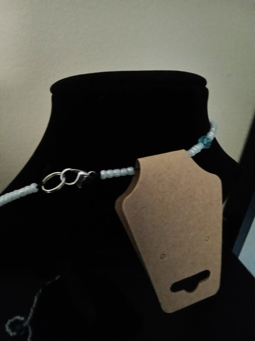 A beaded necklace with light blue seed beads and a silver lobster clasp, displayed on a black velvet jewelry bust.