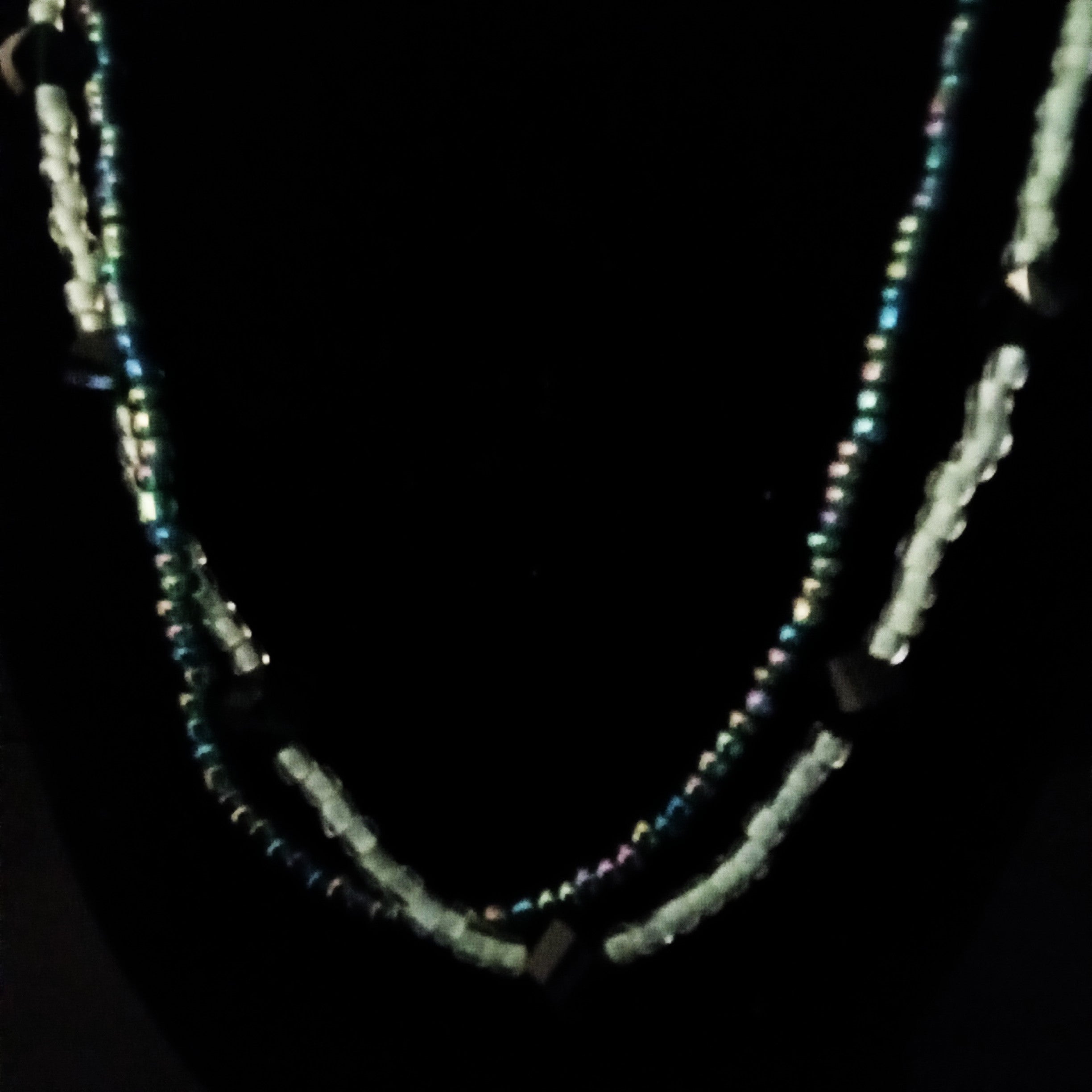A beaded double-strand necklace displayed on a black jewelry bust against a black background. The necklace features iridescent blue-green beads, light mint-green beads, and small dark green cube-shaped beads.