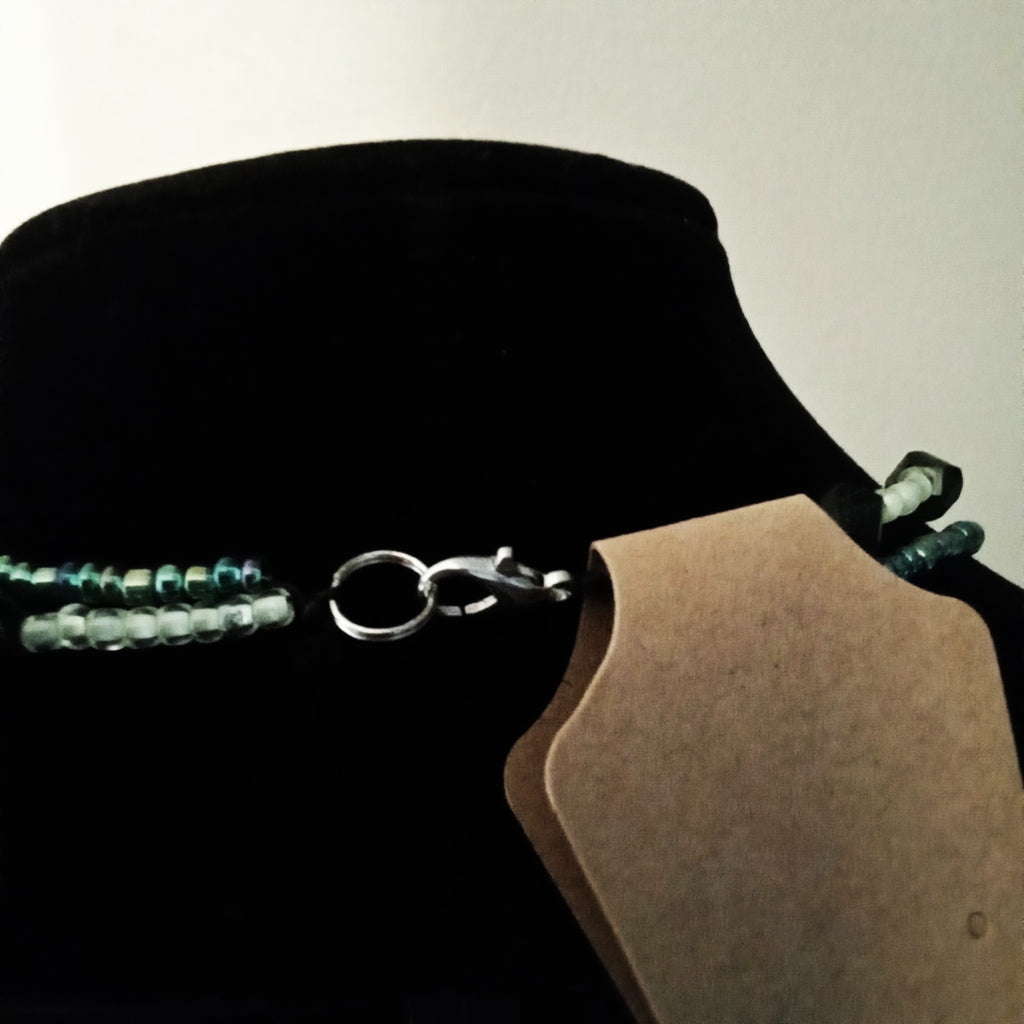 A close-up of a beaded necklace with translucent light blue-green beads and a silver clasp, displayed on a black velvet jewelry bust.