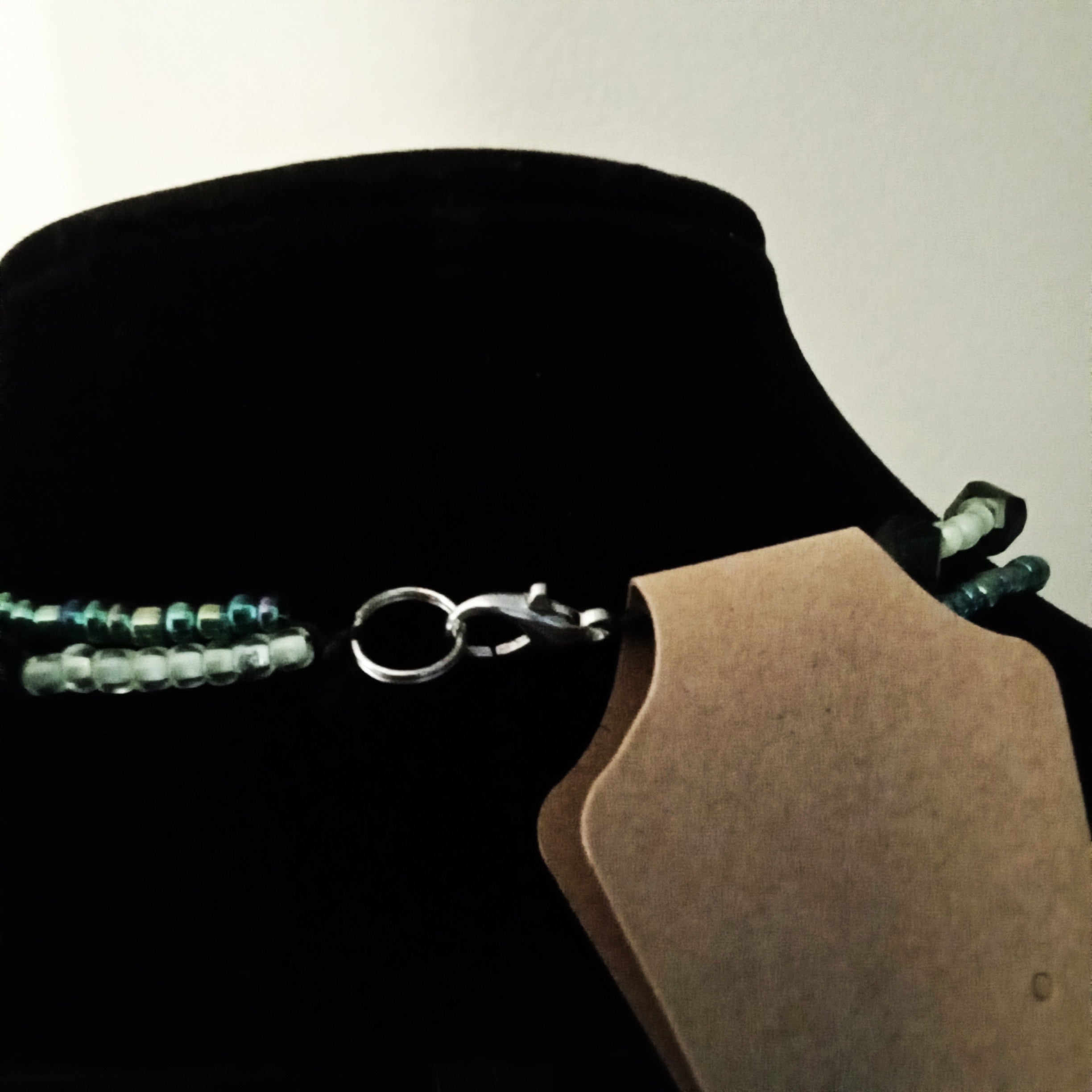 A close-up of a beaded necklace with translucent light blue-green beads and a silver clasp, displayed on a black velvet jewelry bust.