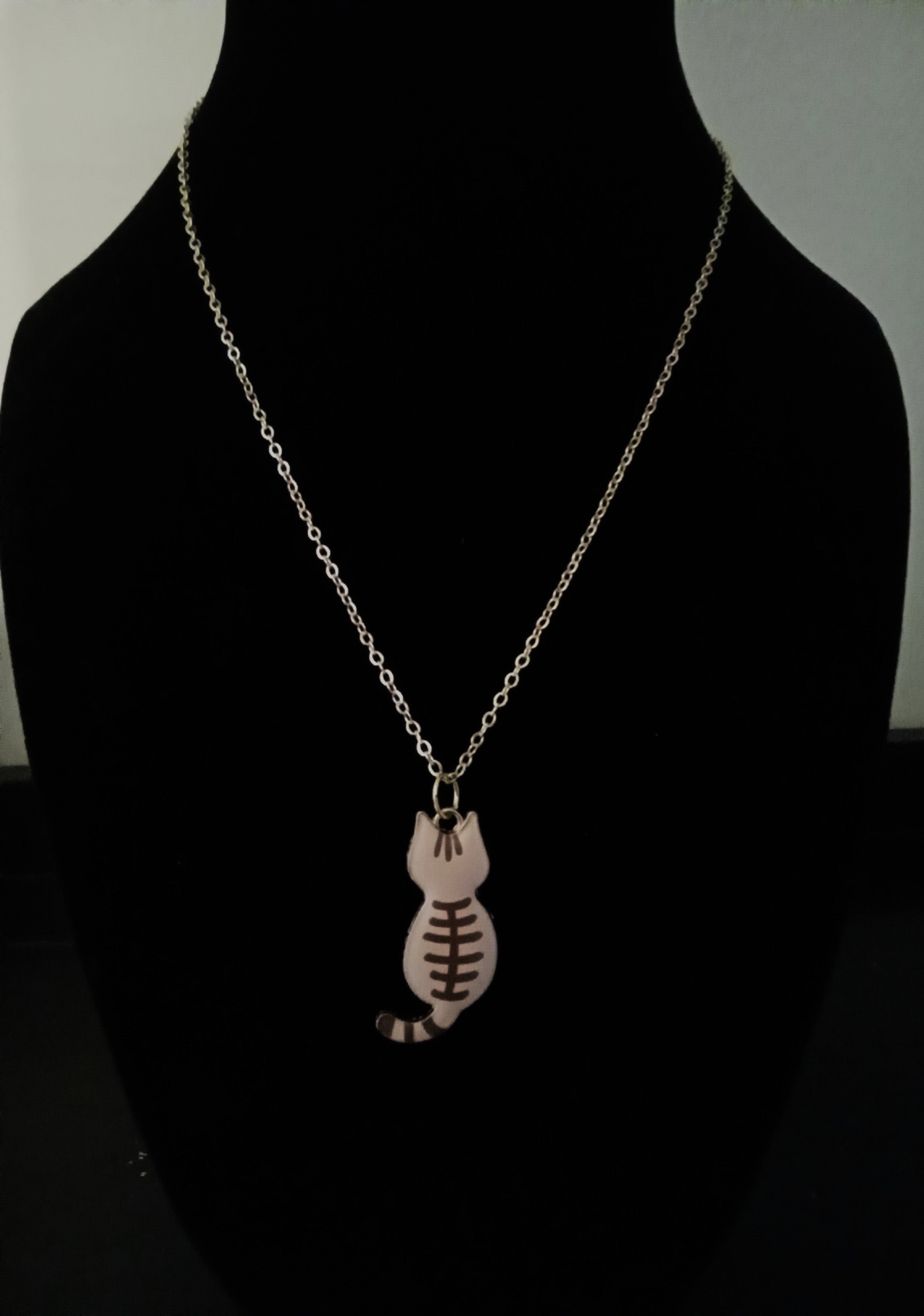 A gold chain necklace with a small cat-shaped pendant featuring a football pattern, displayed on a black mannequin bust.