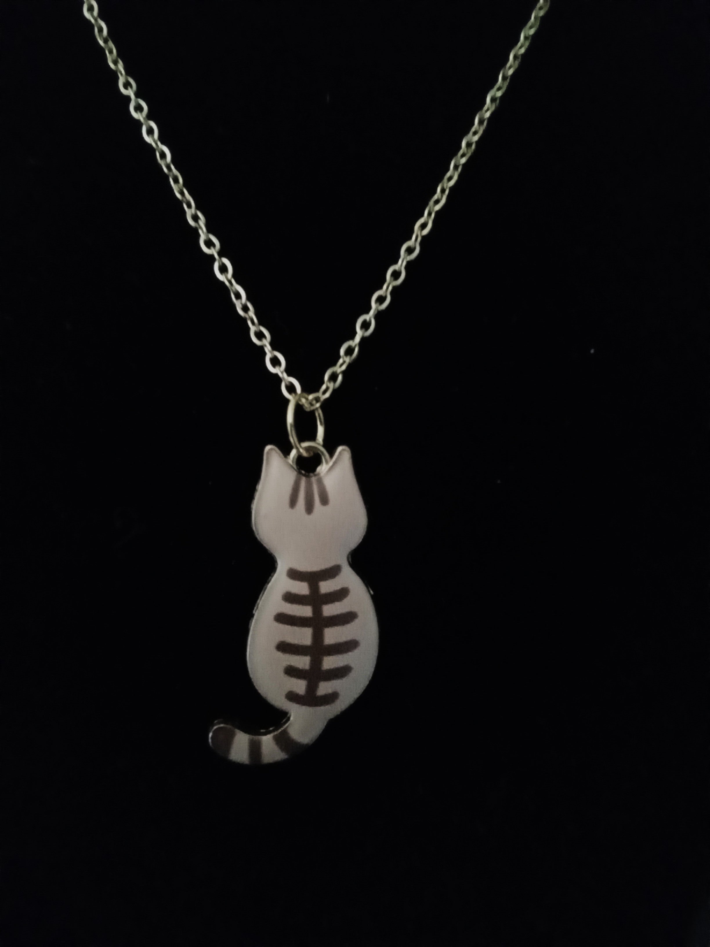 A gold chain necklace featuring a small cat-shaped pendant with a dark brown painted football pattern, shown against a solid black background.