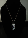 A delicate gold-tone chain necklace with a pendant shaped like a white cat, featuring a purple and green floral design on its body, displayed on a black mannequin bust.