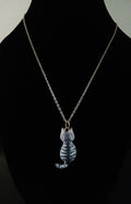 A gold chain necklace with a small cat-shaped pendant featuring gray and white stripes, displayed on a black mannequin bust.