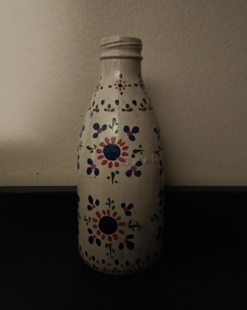 A white glass bottle with a hand-painted folkloric floral pattern in blue, red, and green.