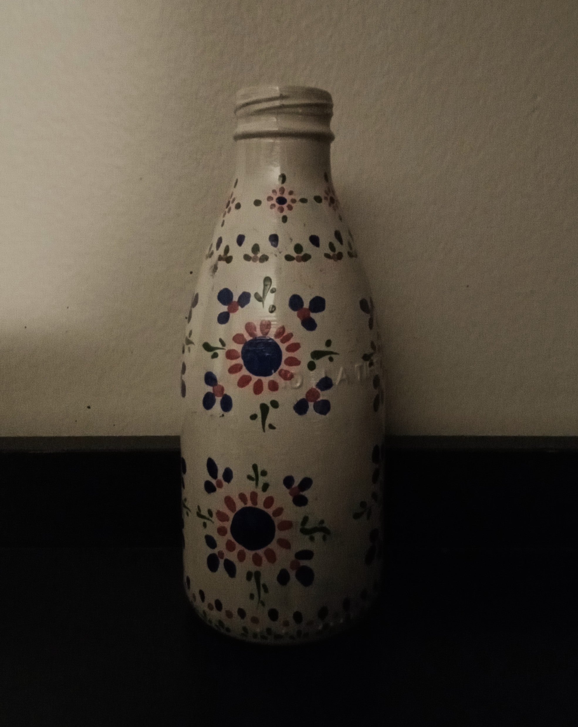 A white glass bottle with a hand-painted folkloric floral pattern in blue, red, and green.