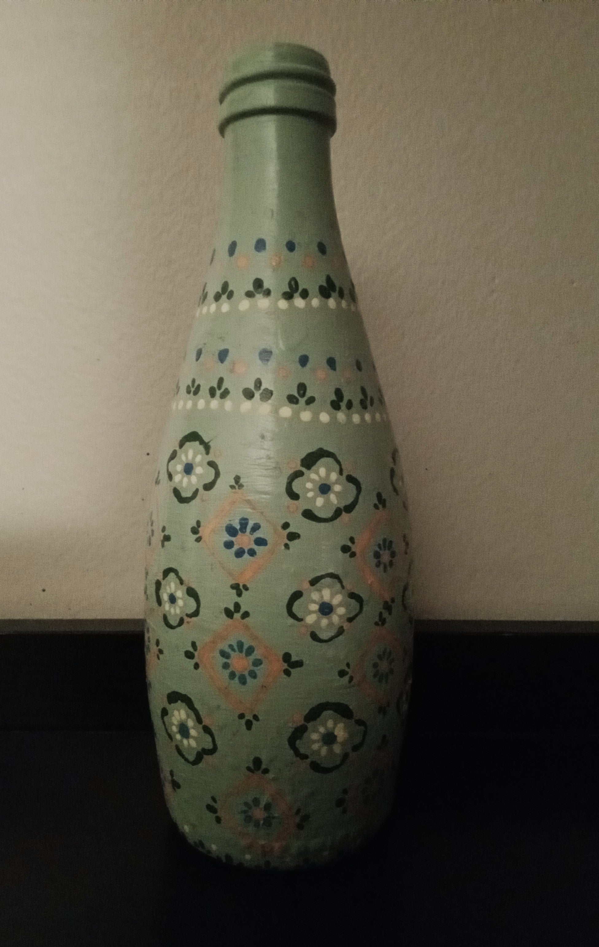 A light sage green glass bottle with a hand-painted floral pattern in dark green, yellow, and orange.