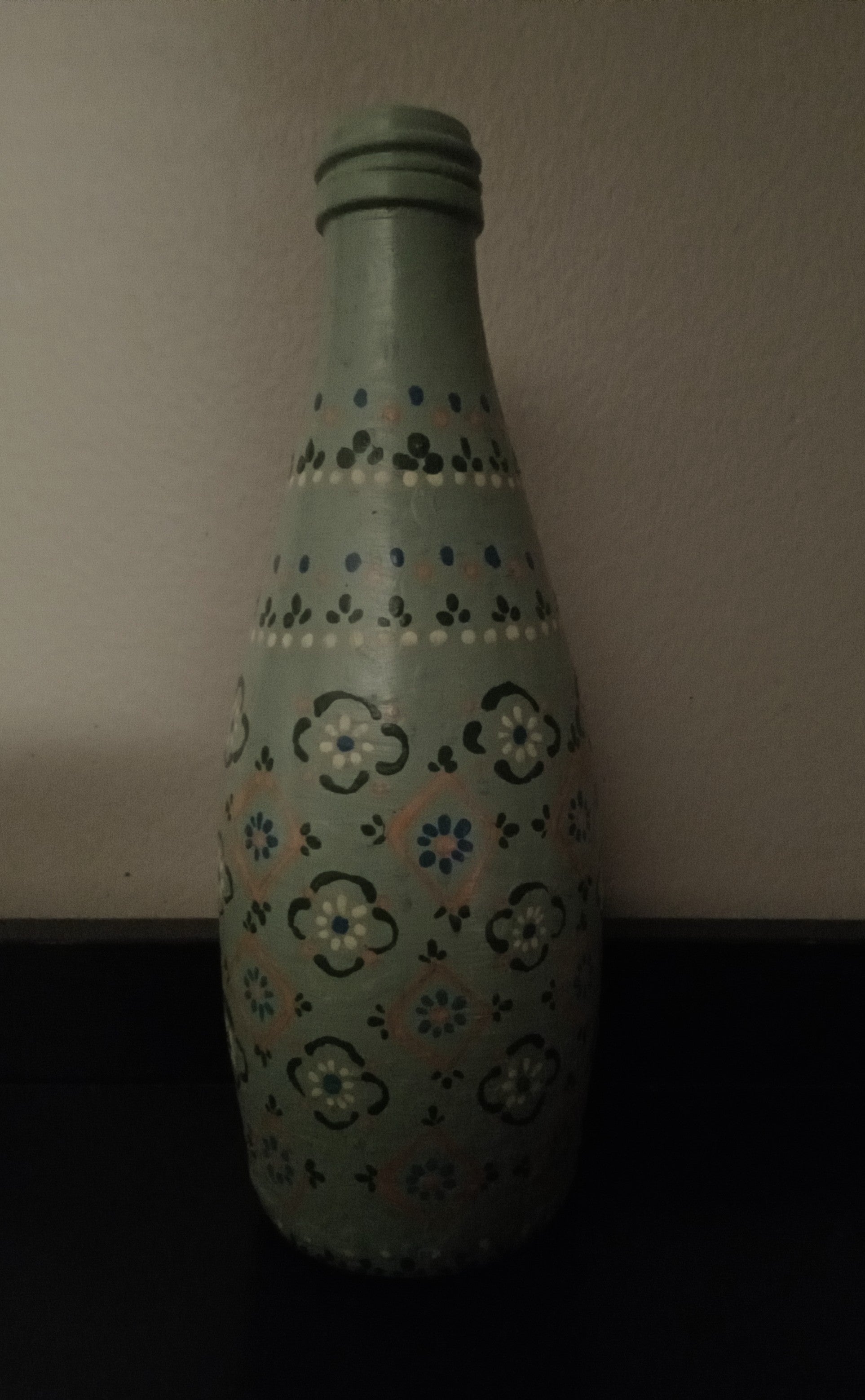 A light sage green glass bottle with hand-painted floral and geometric patterns in blue, yellow, and dark green.