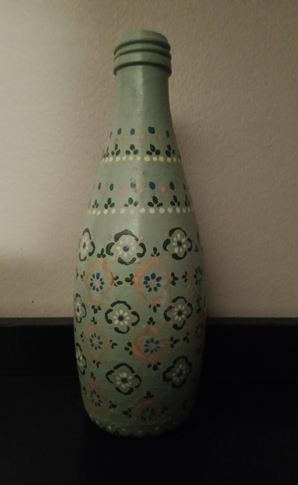 A light green glass bottle with a hand-painted floral pattern in blue, yellow, and orange.