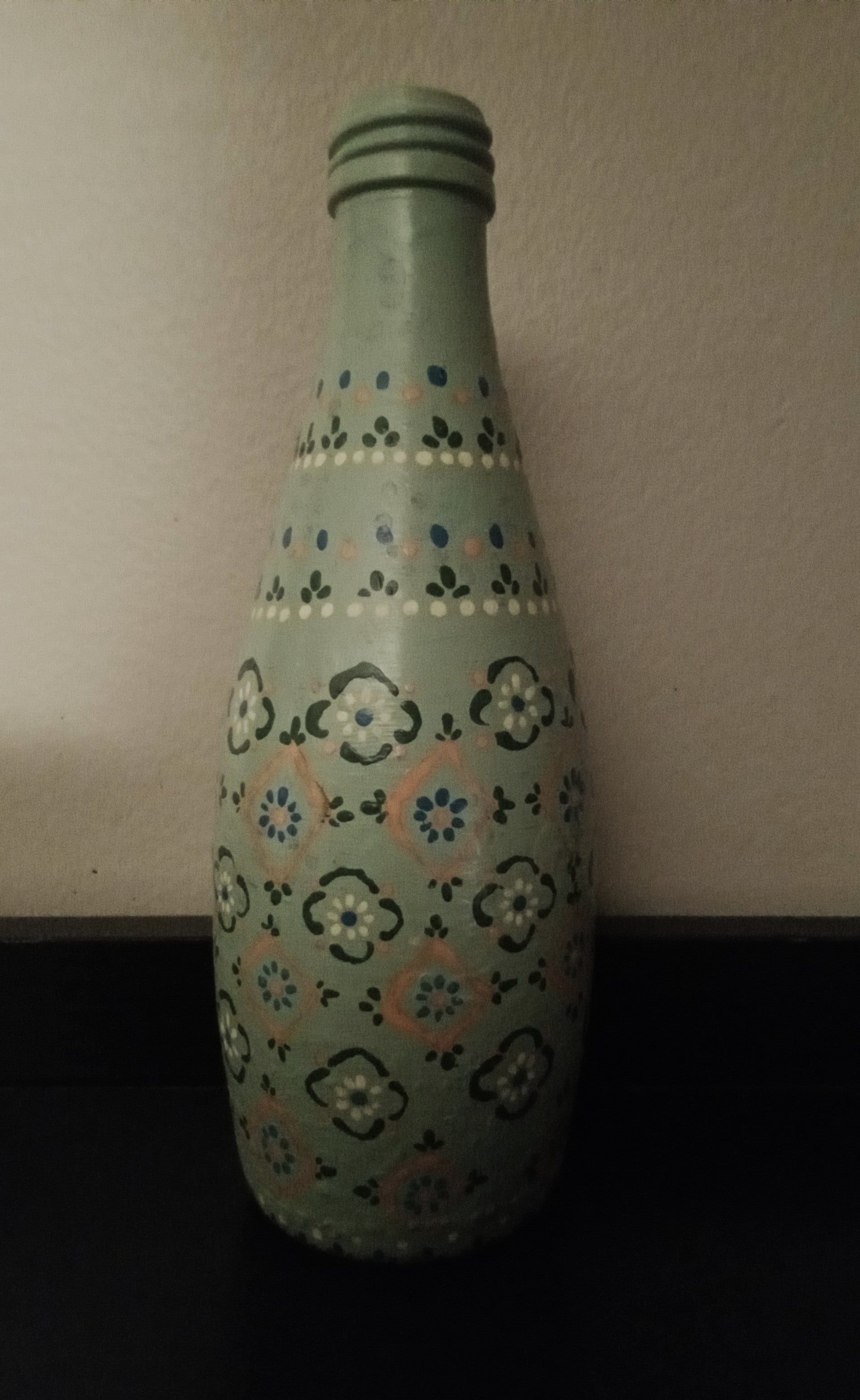 A light green glass bottle with a hand-painted floral pattern in blue, yellow, and orange.