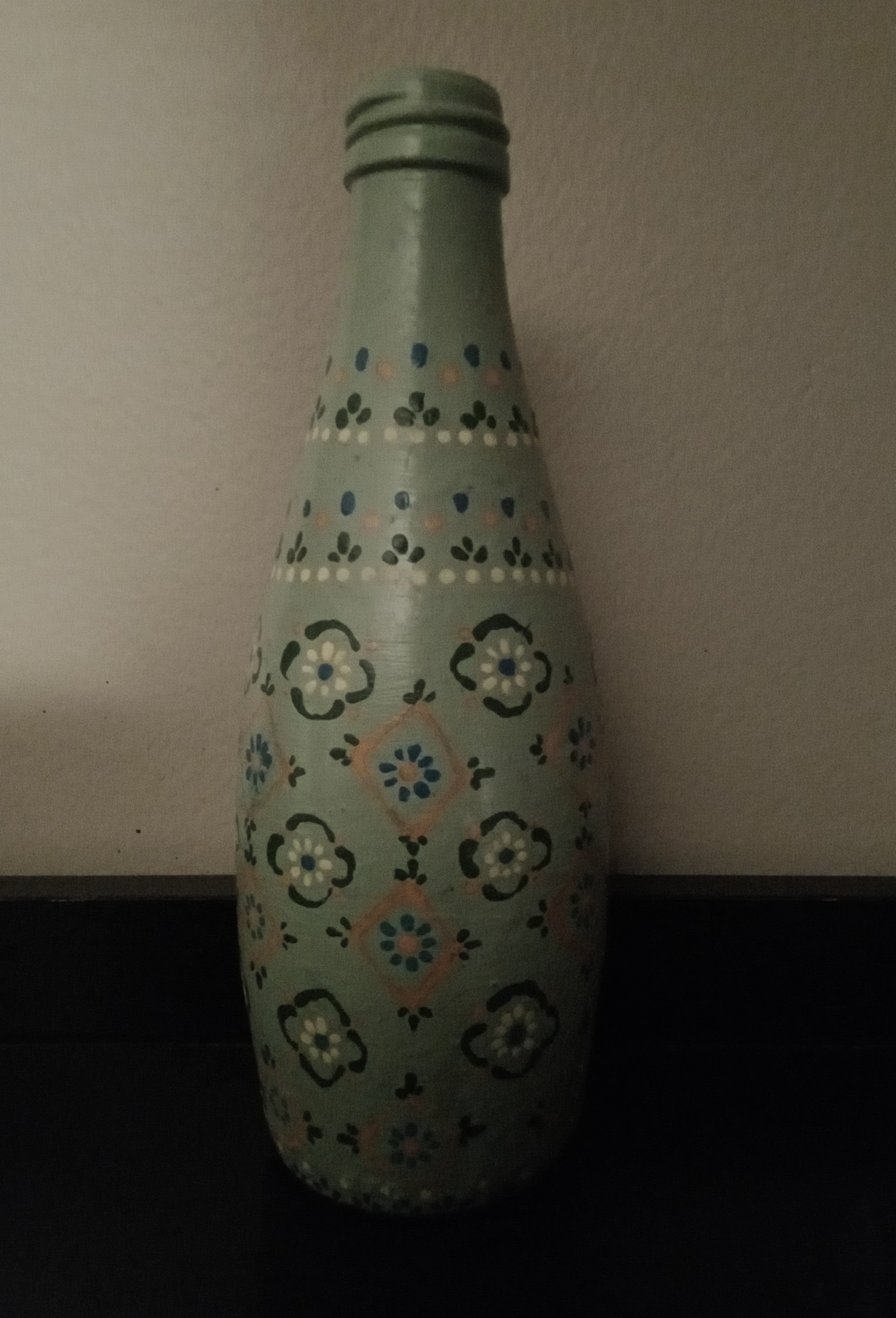 A light green bottle decorated with hand-painted floral and geometric pattern in blue, dark green, yellow, and orange.