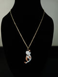 A gold chain necklace with a small cat-shaped pendant, displayed on a black mannequin bust. The pendant is white with orange and black spots, resembling a calico cat.