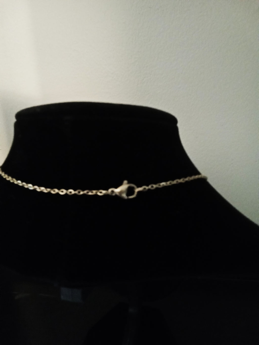 A delicate gold chain necklace with a lobster clasp, displayed on a black velvet jewelry bust.