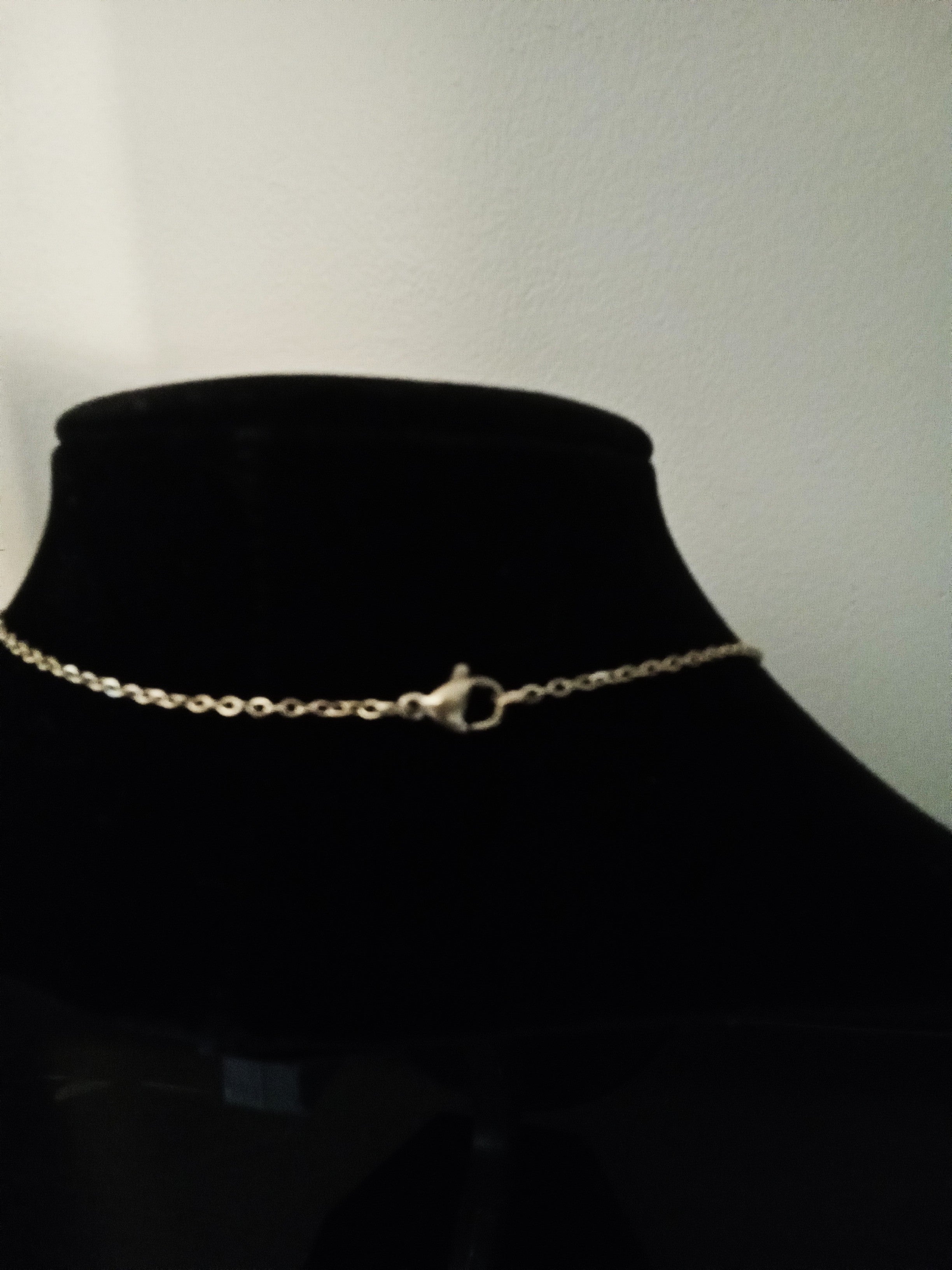 A delicate gold chain necklace with a lobster clasp, displayed on a black velvet jewelry bust.