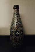 A black glass bottle decorated with intricate hand-painted Aboriginal-style dot art patterns in yellow, green, orange, and light blue.