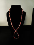 A long, beaded necklace with alternating red and orange beads, displayed on a black velvet jewelry bust against a plain light background.