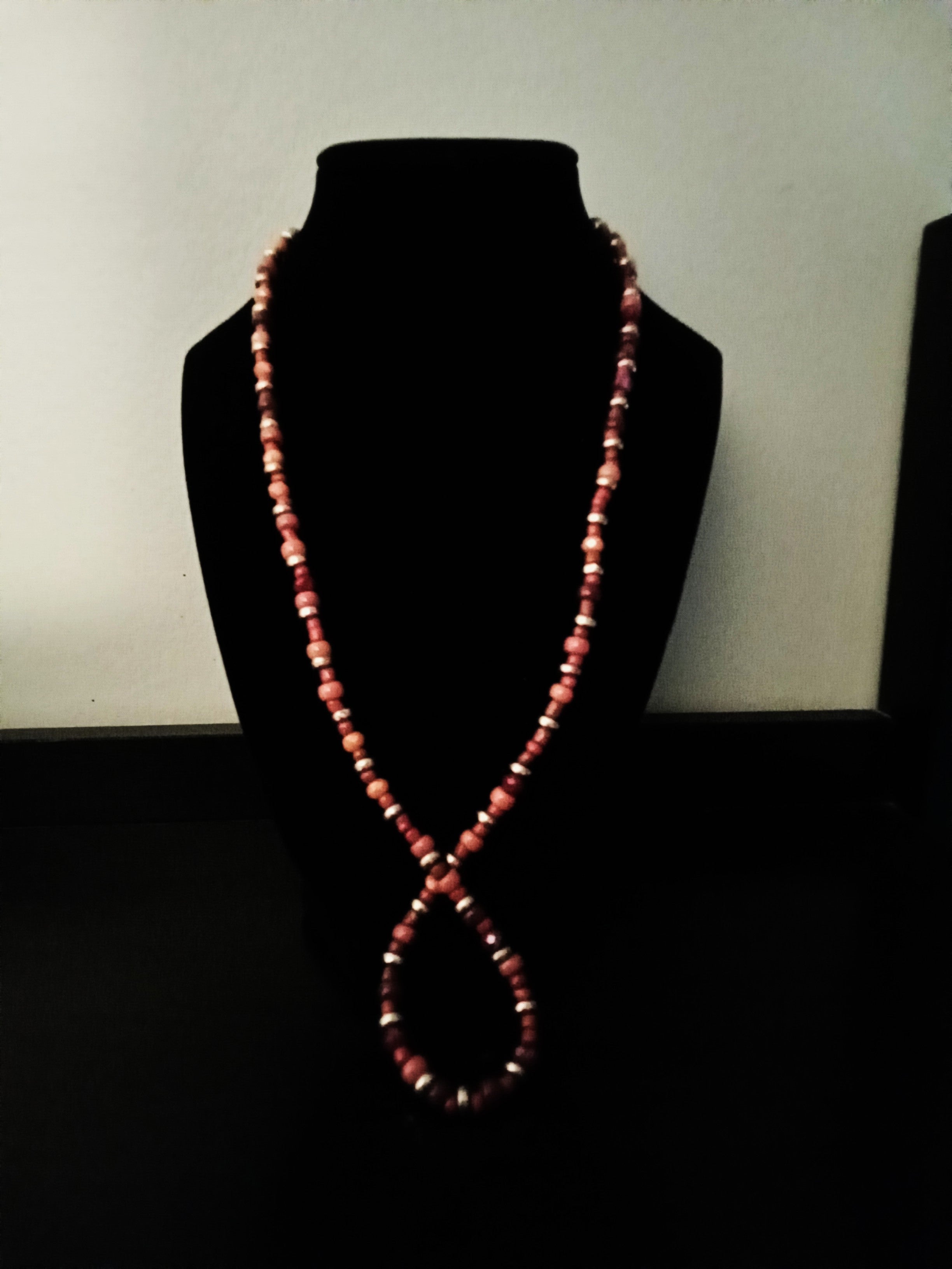A long, beaded necklace with alternating red and orange beads, displayed on a black velvet jewelry bust against a plain light background.