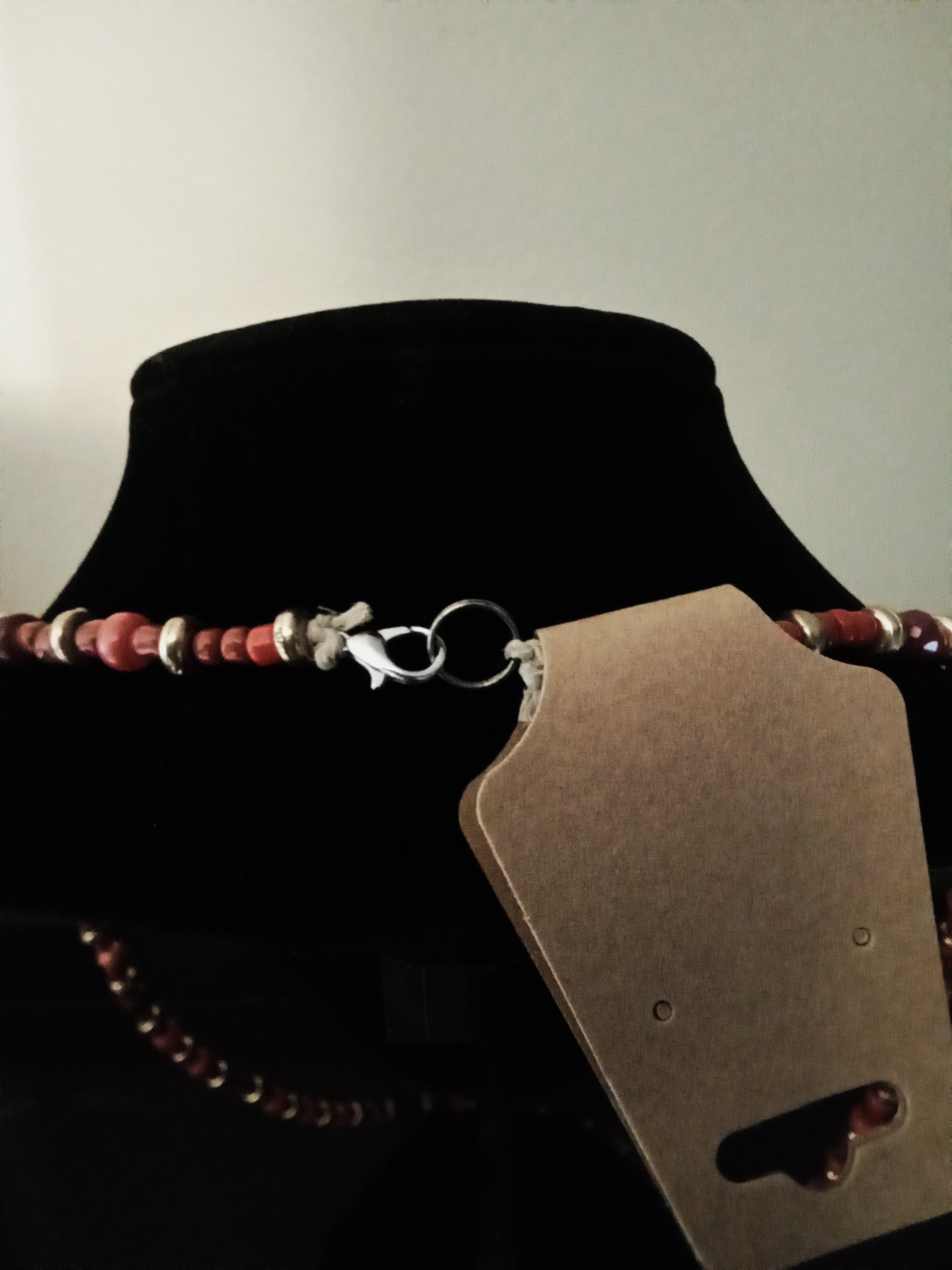 A beaded necklace with reddish-brown and orange beads, gold-toned spacer beads, and a silver lobster clasp, displayed on a black velvet jewelry bust.