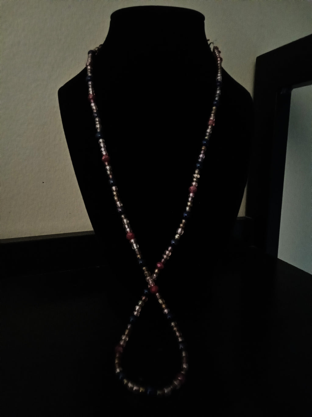 A long, beaded necklace displayed on a black velvet mannequin bust against a dark background.