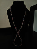 A long, beaded necklace displayed on a black velvet mannequin bust against a dark background.