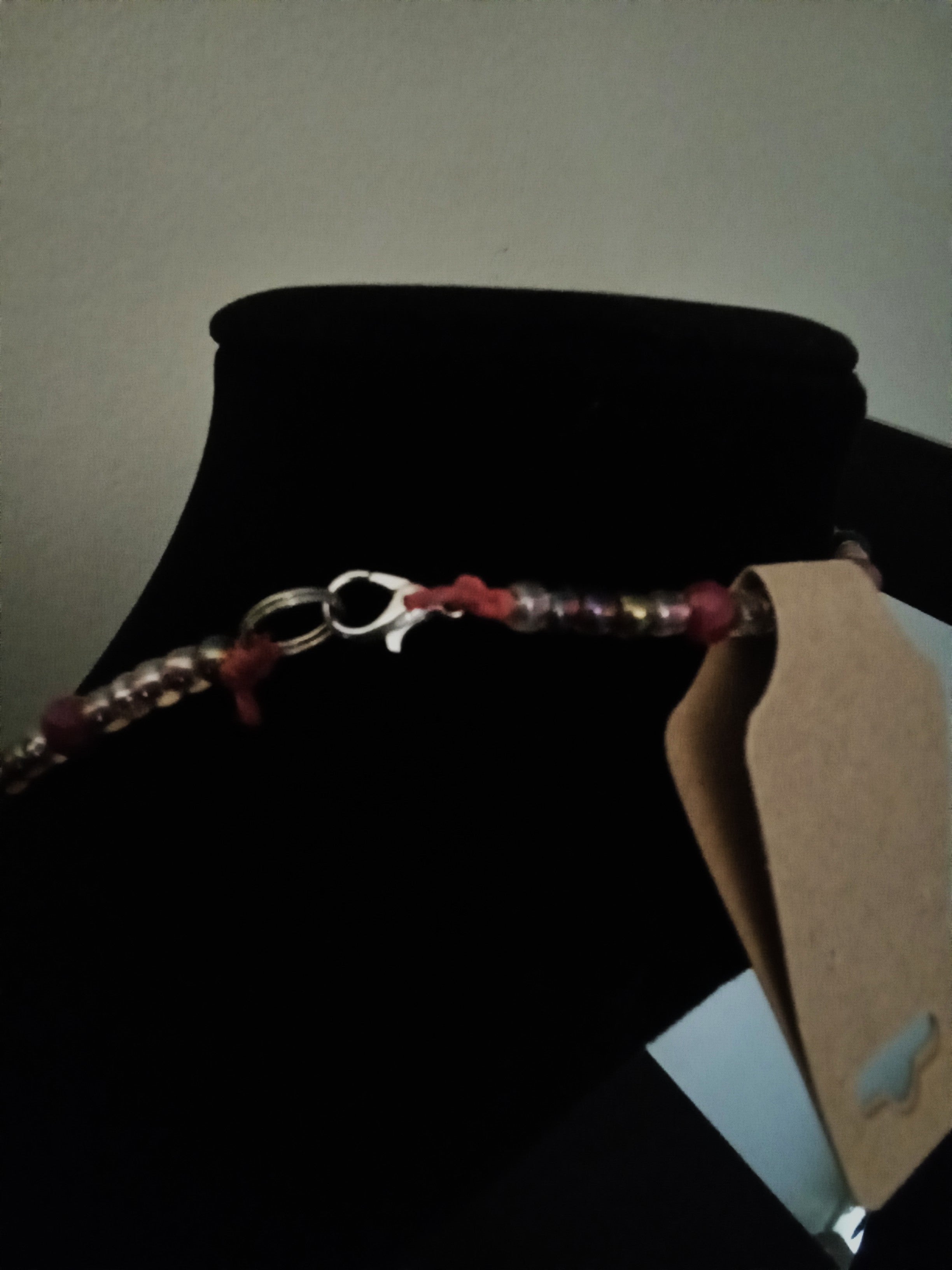 A beaded necklace with red, purple, and light pink beads, and a silver lobster clasp, displayed on a black jewelry bust.