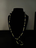 A long, beaded necklace with dark blue and yellow beads displayed on a black mannequin bust.