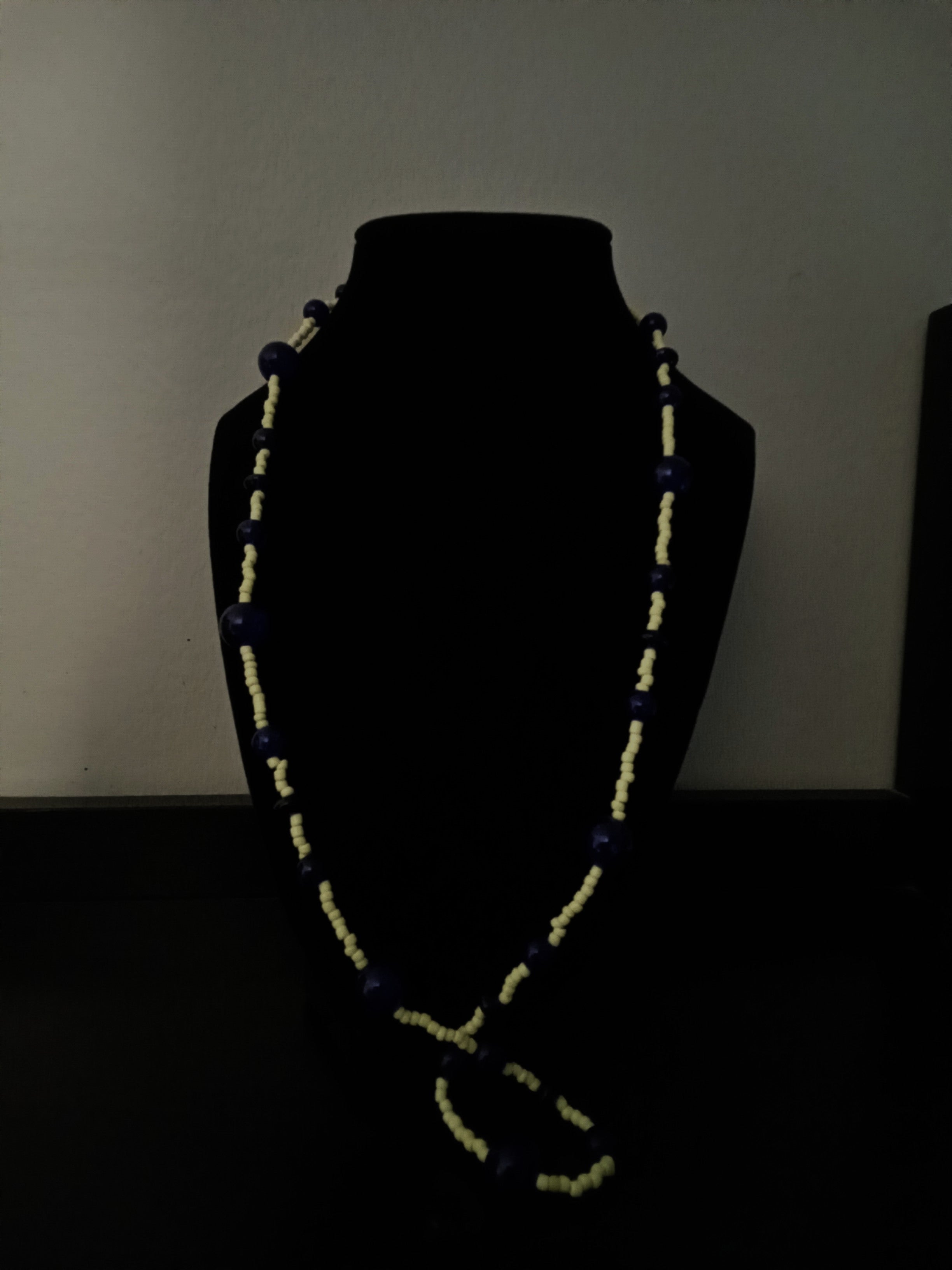 A long, beaded necklace with dark blue and yellow beads displayed on a black mannequin bust.