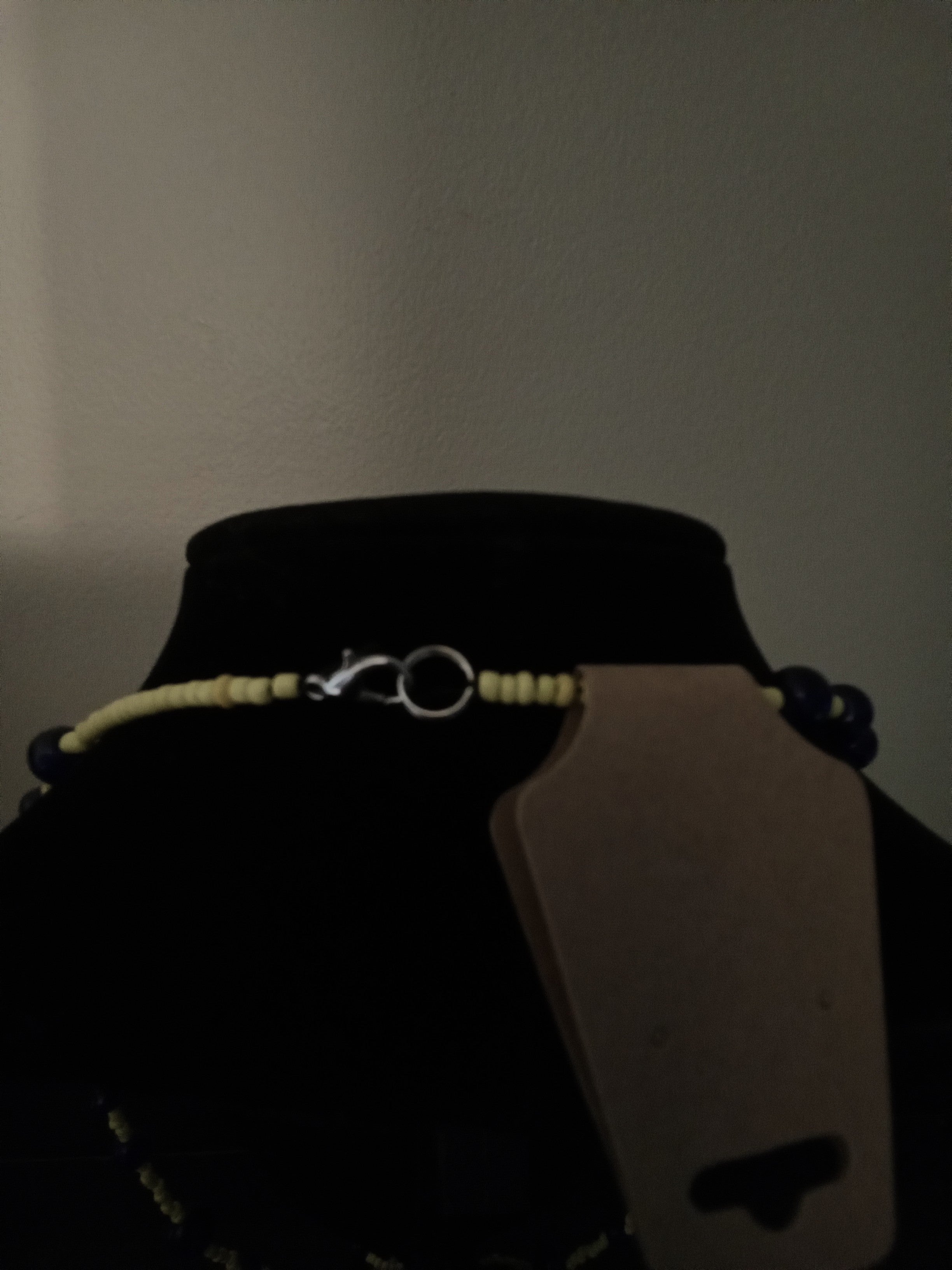 A beaded necklace with yellow beads, dark blue beads, and a silver clasp, displayed on a black mannequin bust.