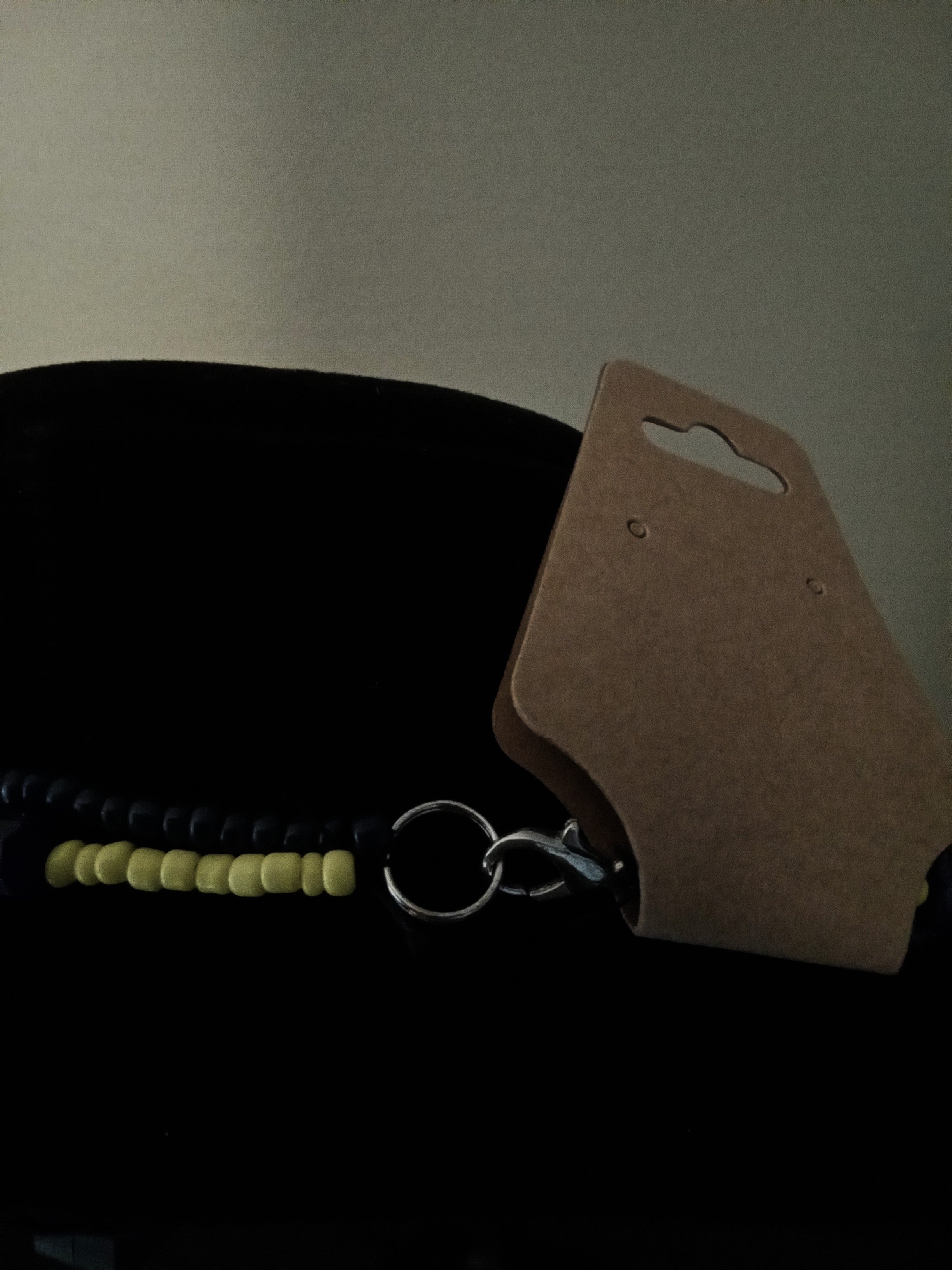 A close-up of a dark blue and yellow necklace with a silver metal clasp, photographed against a dark background.