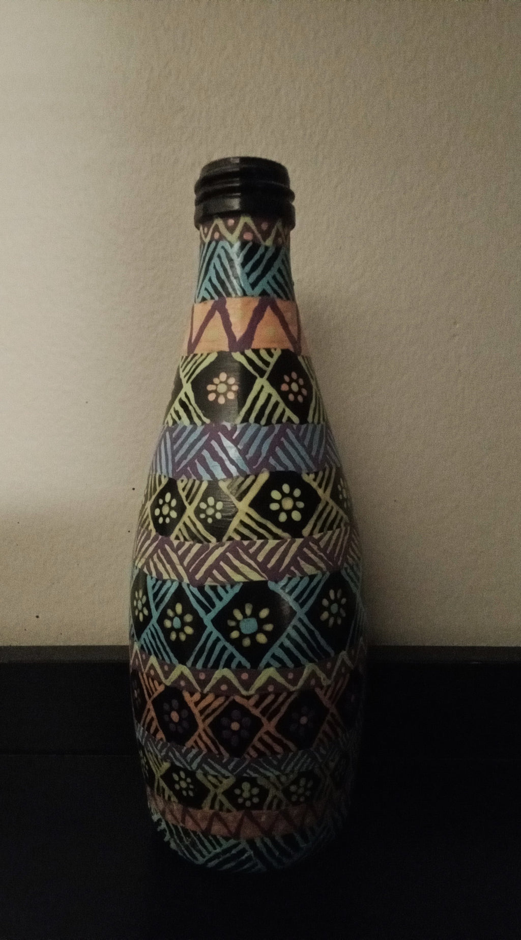 A decorative bottle covered in a colorful geometric tribal-style pattern of blue, yellow, pink, green, and orange.