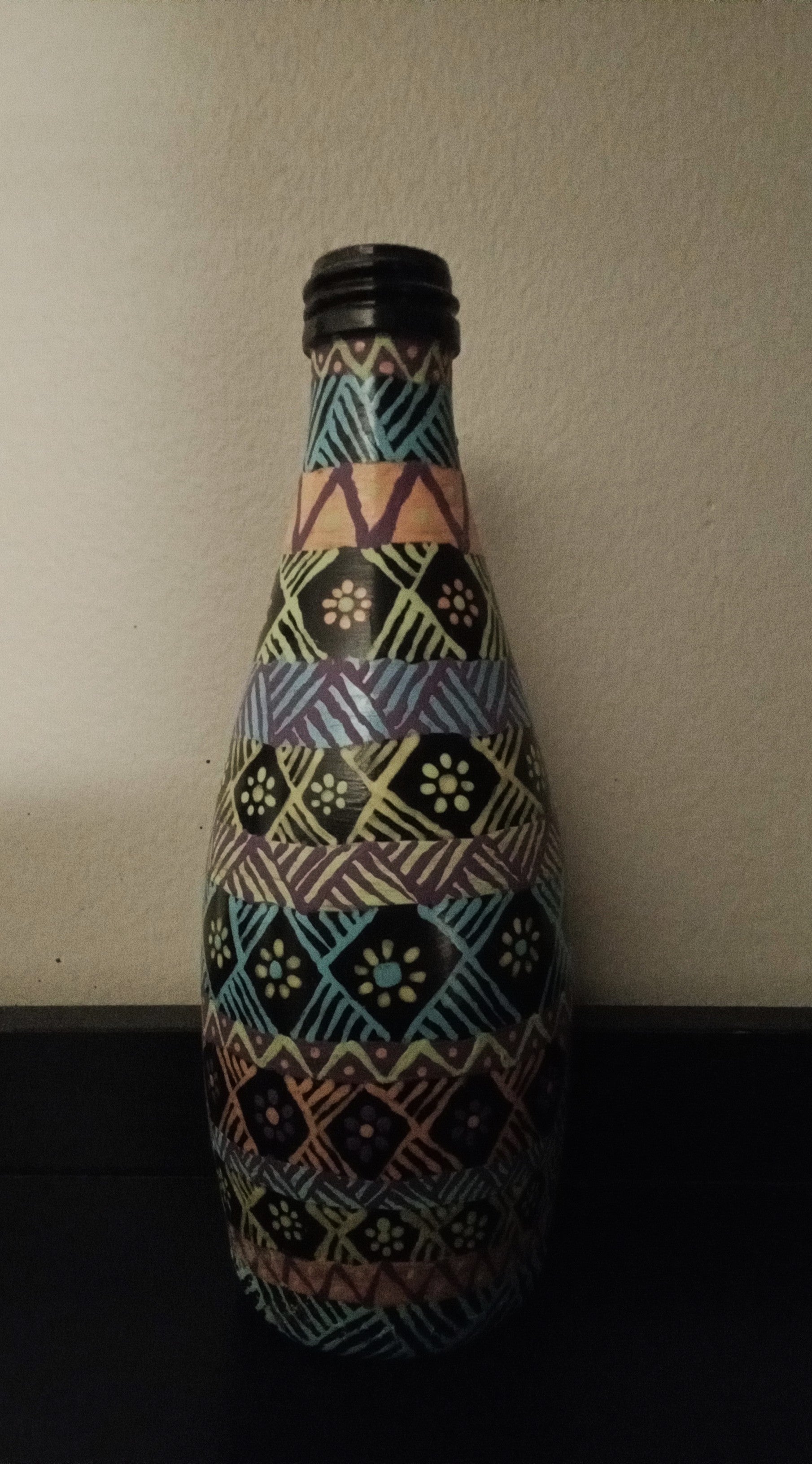 A decorative bottle covered in a colorful geometric tribal-style pattern of blue, yellow, pink, green, and orange.